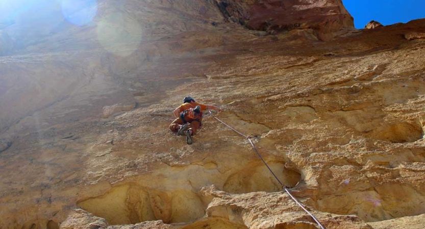 Wearing safety gear and secured by ropes, a person climbs a steep rock wall.